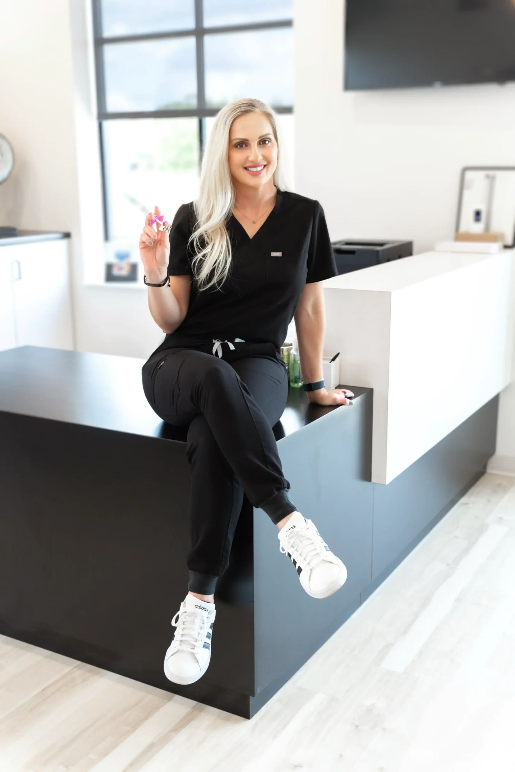Female aesthetic practitioner in black scrubs smiling in clinic