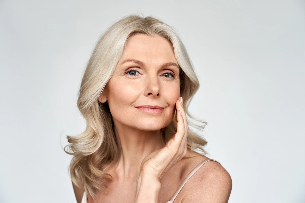 Mature woman with smooth, radiant skin touching her cheek following a post-procedure skincare routine