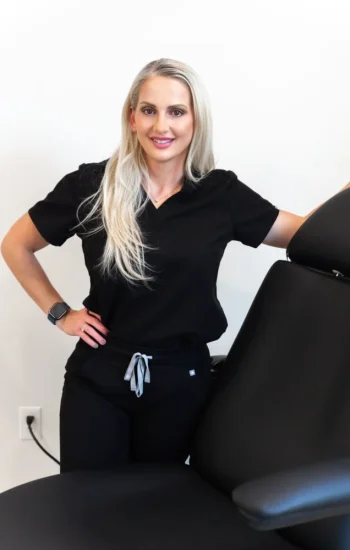 Professional cosmetic nurse in black scrubs smiling by treatment chair