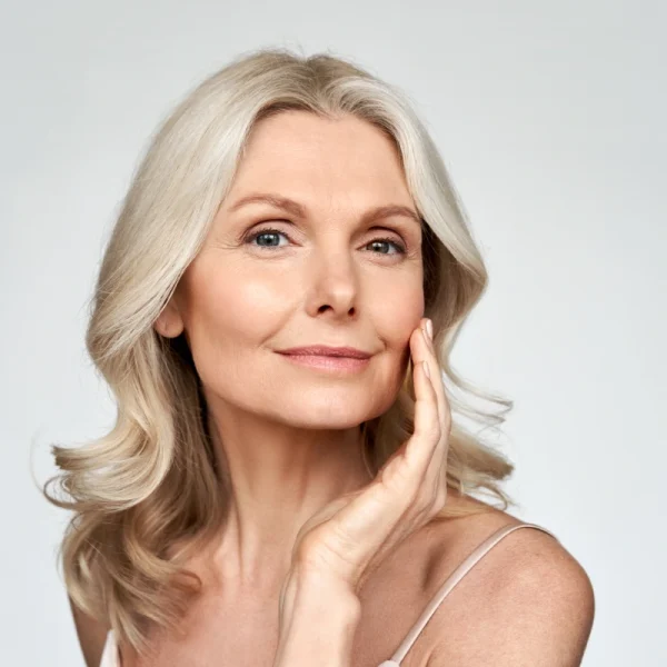 Mature woman with smooth, radiant skin touching her cheek following a post-procedure skincare routine